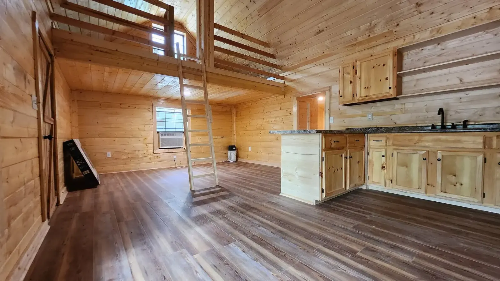 Wood-finished A-frame cabin interior with loft and kitchen
